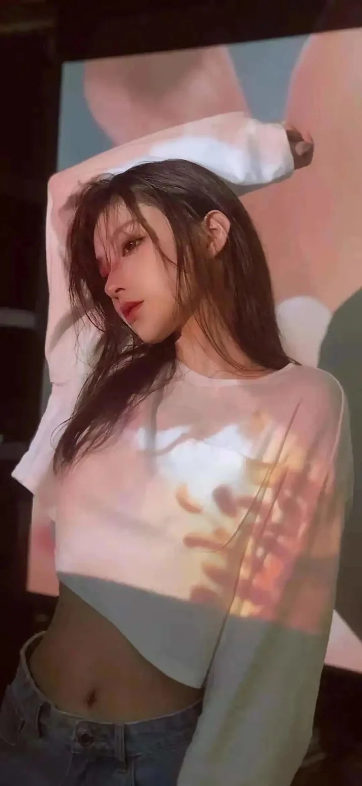 一名长发女性穿着浅色长袖上衣，身上映着柔和彩色的投影光影。