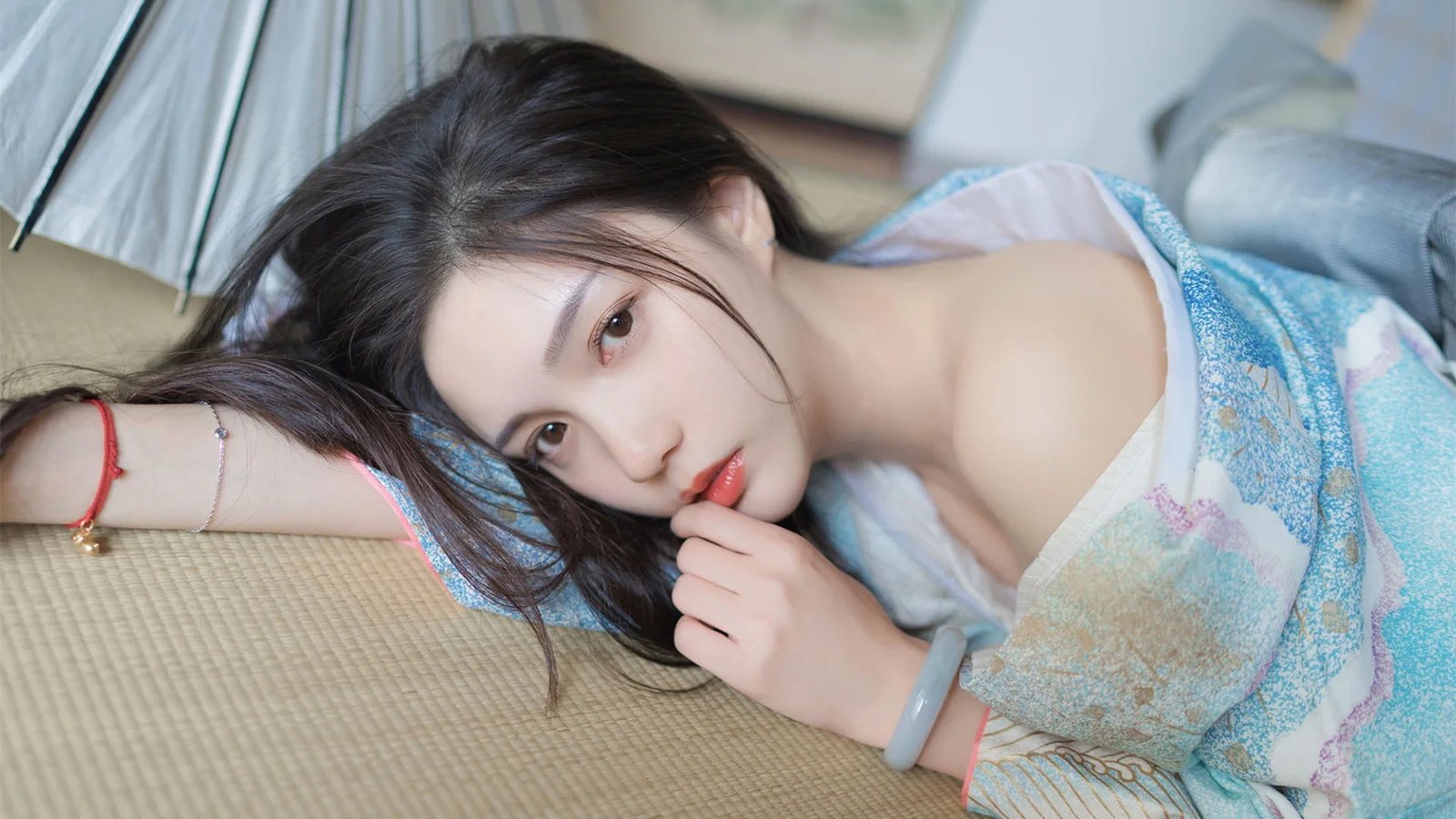 一名成年女性侧卧在榻榻米上，身穿浅蓝色印花服饰，凝视镜头。