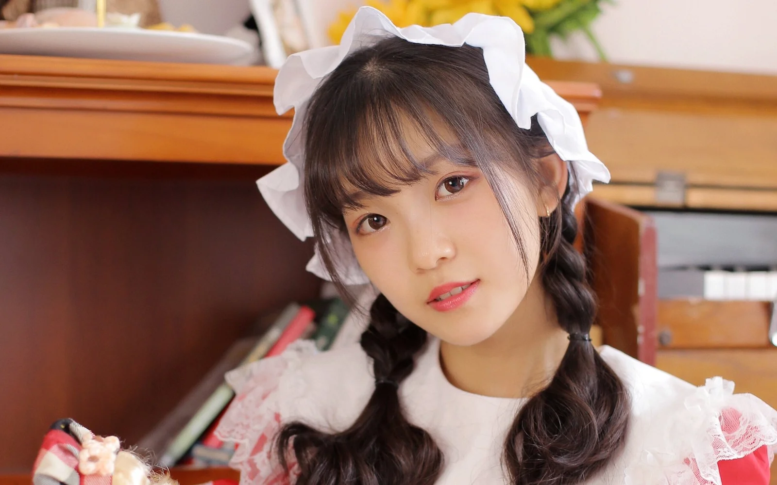 白いリボンをつけた三つ編みの若い女性が、室内でカメラに微笑みかけています。