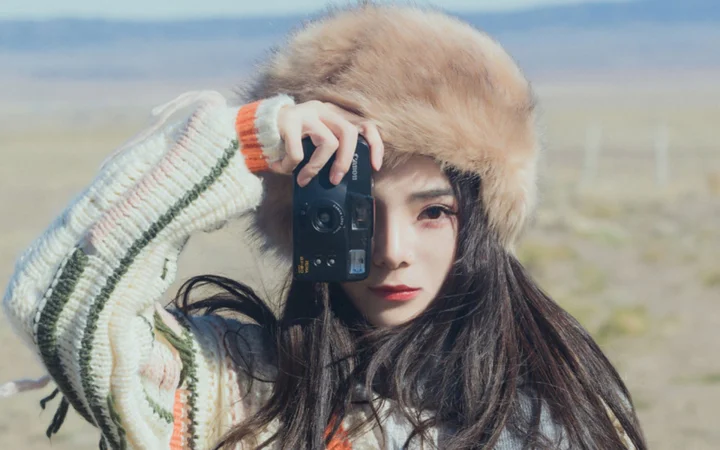 一名戴着毛绒帽子的女子在户外用相机遮住部分脸庞。