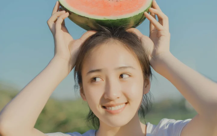 一位微笑的女子在户外将半块西瓜举在头顶。