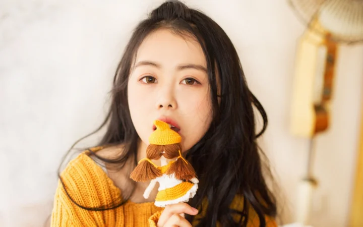 長い髪の女性がアイスクリームのデザートを口元に持ち、カメラを見つめている。