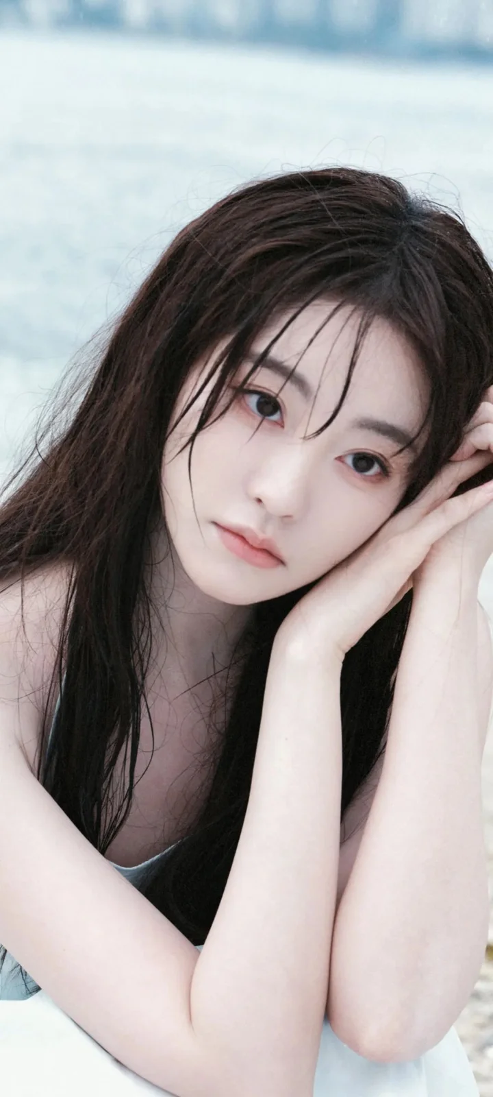 一名长发女性用双手托着脸颊，面向镜头拍摄近距离肖像。