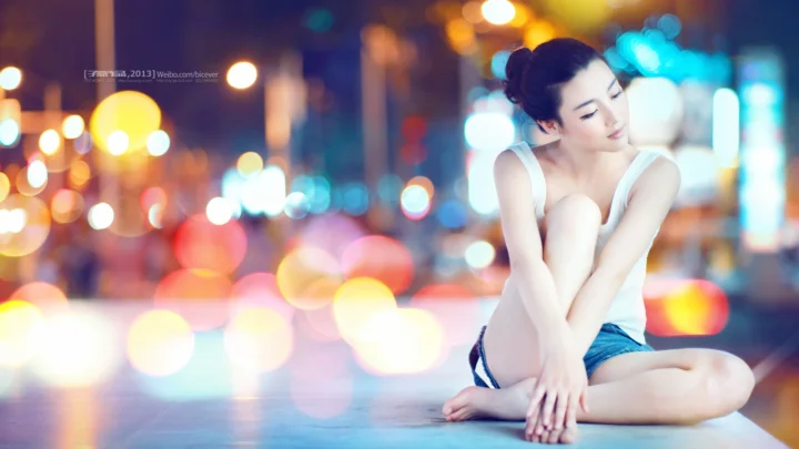 一名成年女子坐在地面上，身后是虚化的彩色城市灯光。