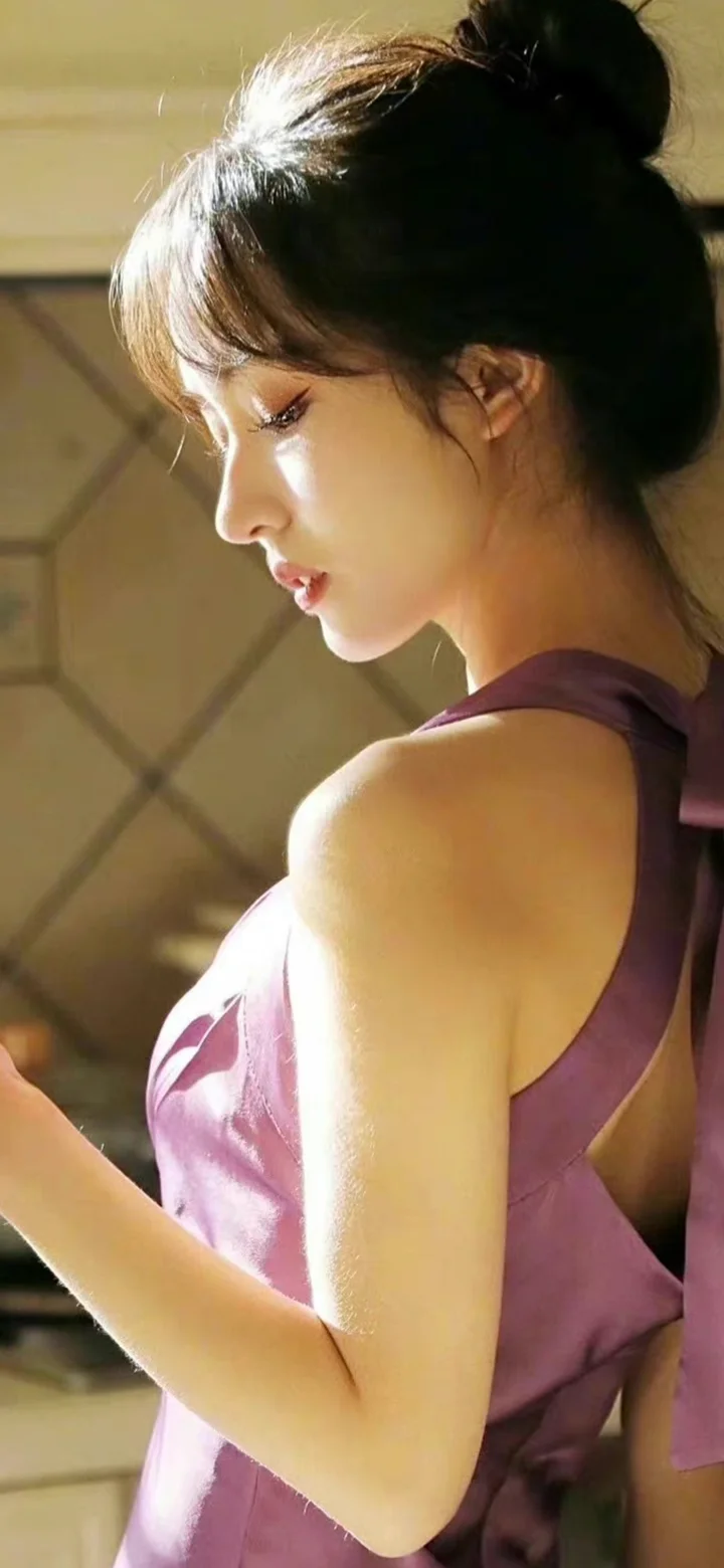 一名身穿粉色无袖裙装的成年女性在室内侧身面向左侧。