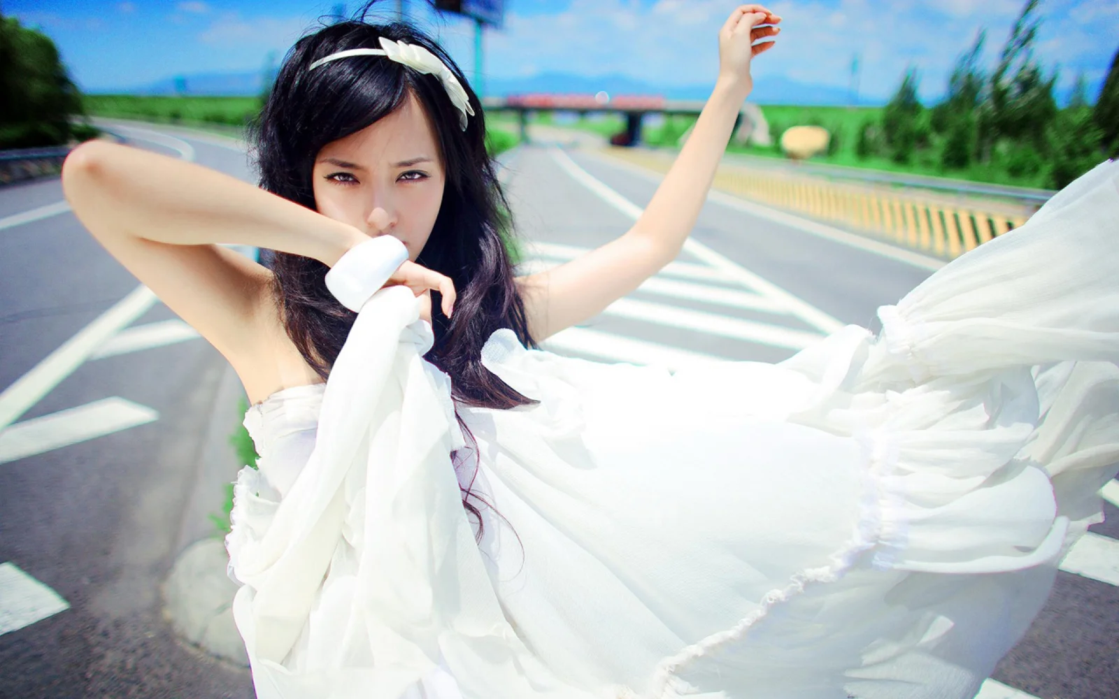 白いドレスを着た女性が道路の上でポーズを取っている。
