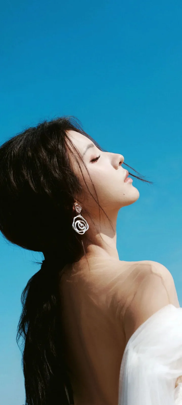 一位成年女性在蓝色天空背景前呈现侧脸轮廓，佩戴圆形耳饰。