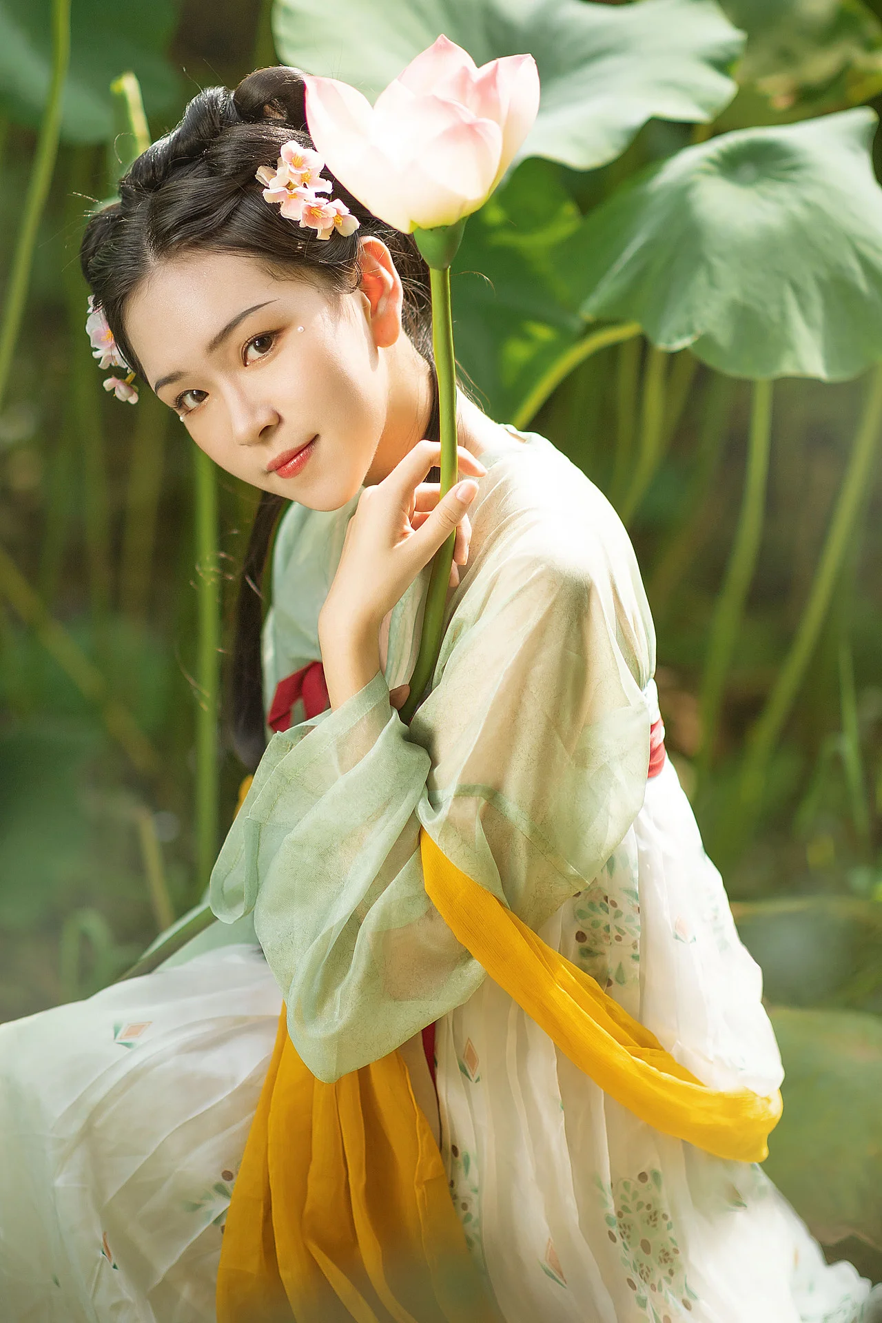 一位身穿傳統服飾的女子手持荷花，站在綠葉環繞的戶外環境中。