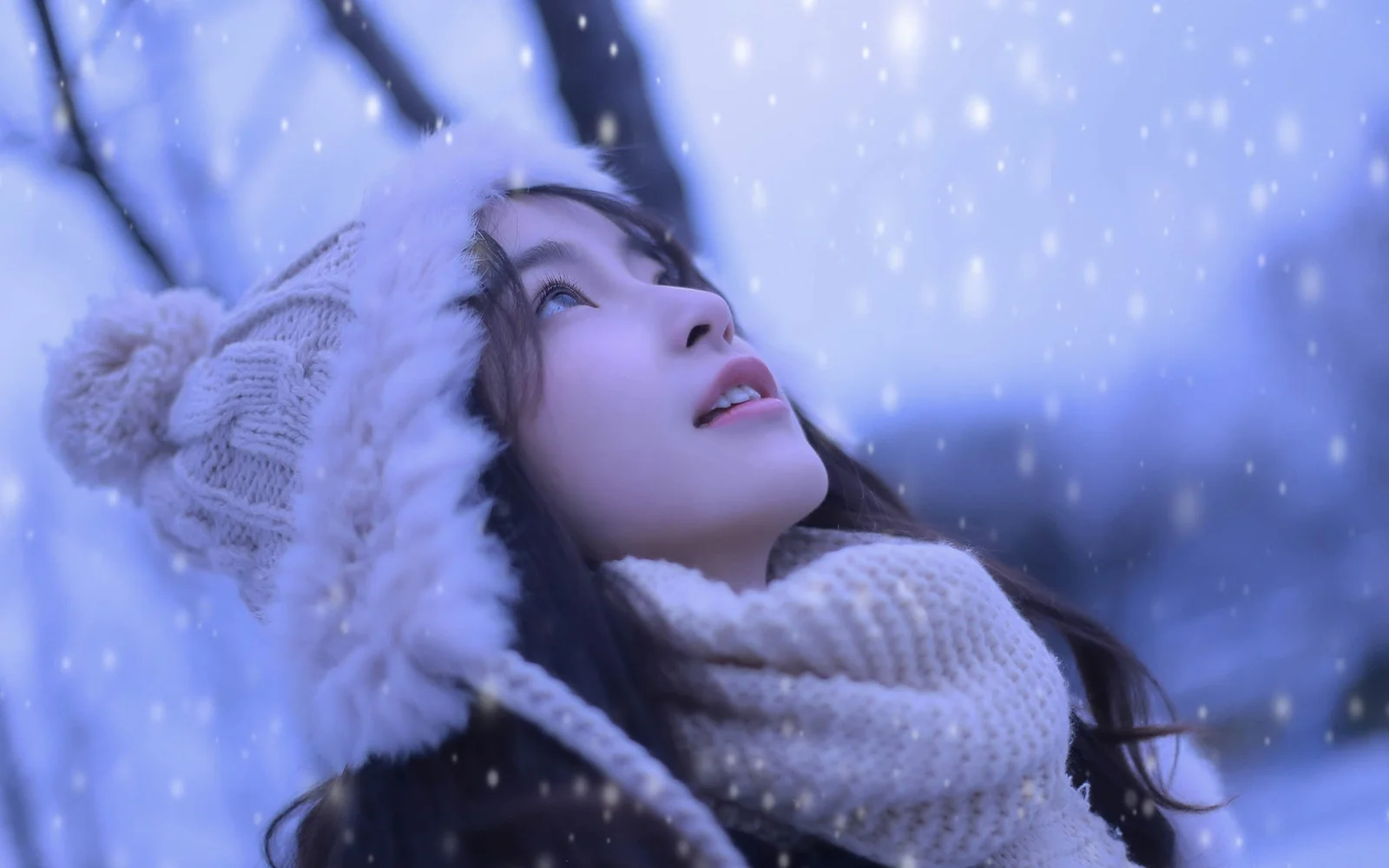 ニット帽とマフラーを身につけた女性が降り積もる雪を見上げている。