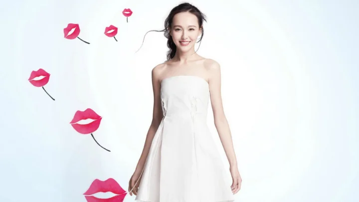 一名成年女性身穿白色无肩带连衣裙站在浅色背景前，周围点缀着红色嘴唇图案。