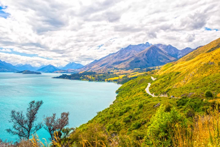 湛蓝湖水、群山、金色山坡和蜿蜒道路构成壮丽的自然风景。