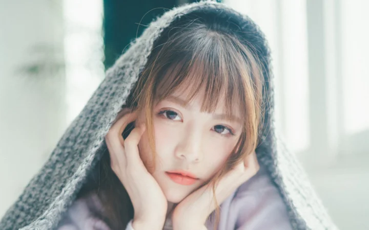 一名女性在柔和室内光线下裹着灰色毯子直视镜头。