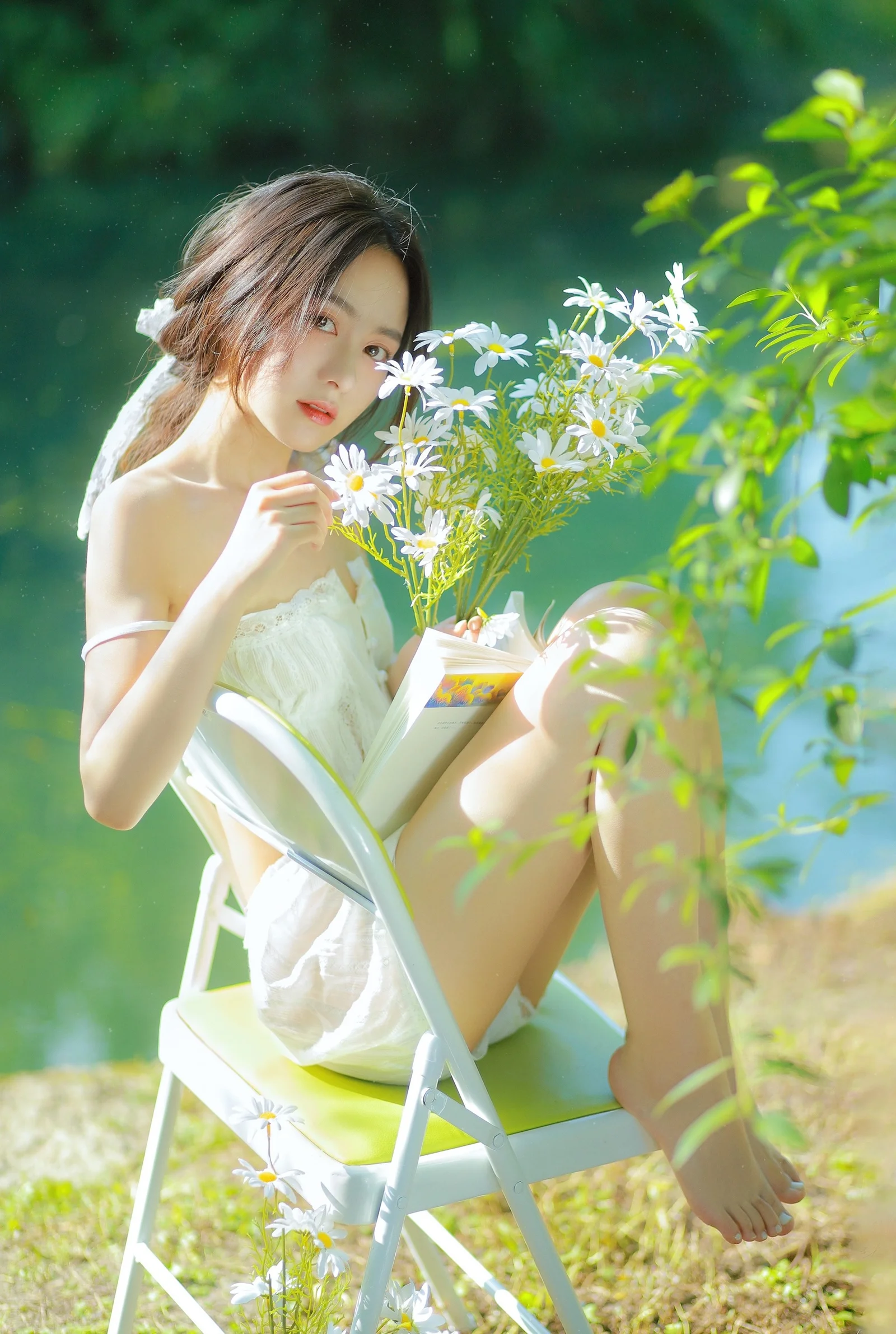 한 여성이 야외 의자에 앉아 책과 흰 데이지 꽃다발을 들고 햇살을 받고 있습니다.