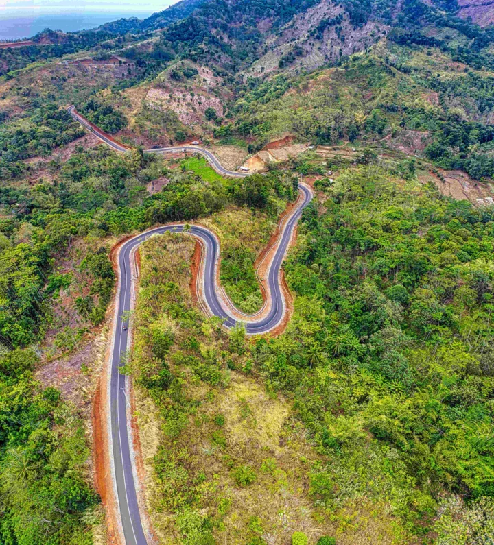 蜿蜒的公路穿过郁郁葱葱的山地森林，远处可见层叠山坡和海岸线。