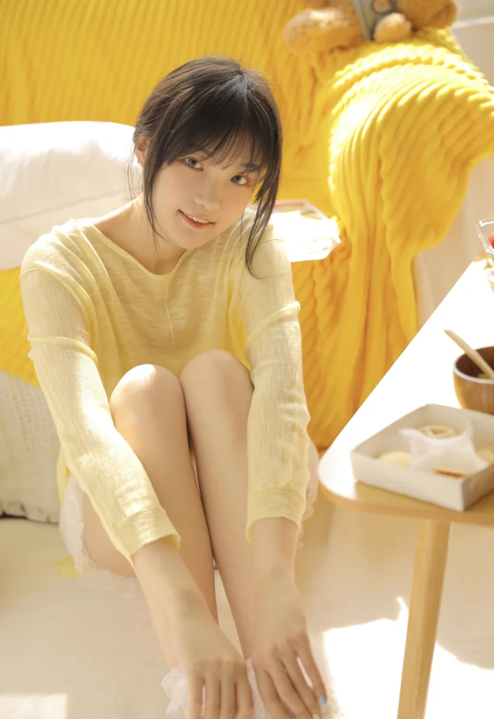一名年轻女子坐在明亮的黄色室内空间中，面向镜头微笑。