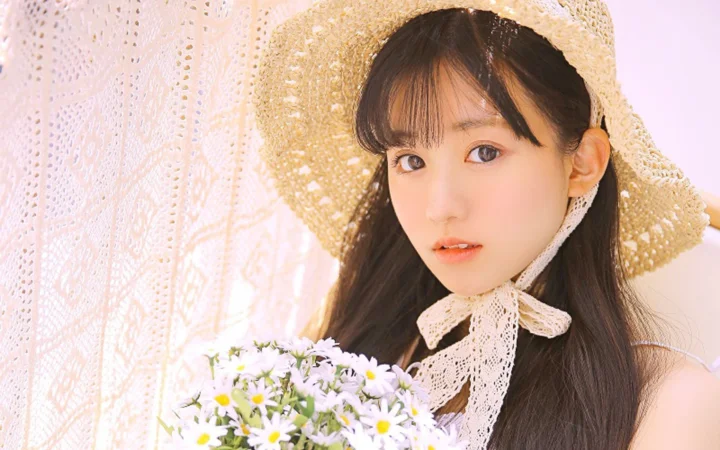 짜임이 있는 밀짚모자를 쓴 여성이 부드러운 레이스 커튼을 배경으로 데이지 꽃다발을 들고 있습니다.