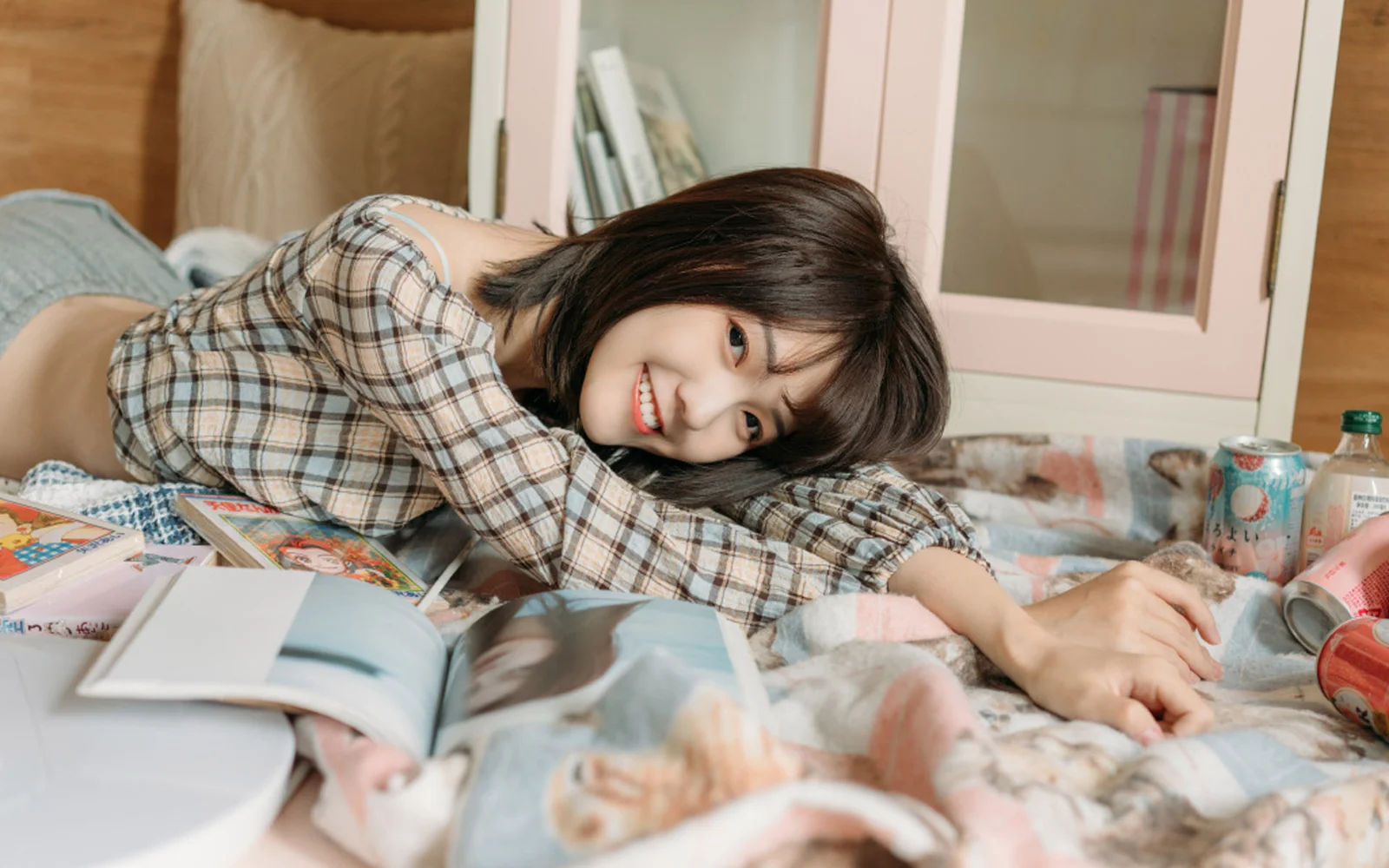 一名微笑的女性穿著格紋襯衫趴在床上，身旁放著一本打開的雜誌。