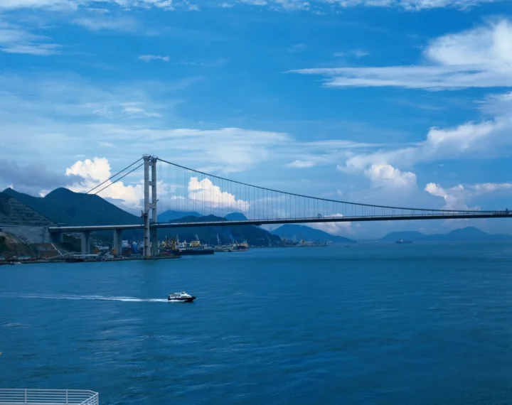 一座悬索桥横跨蓝色海湾，远处是群山与晴朗天空。