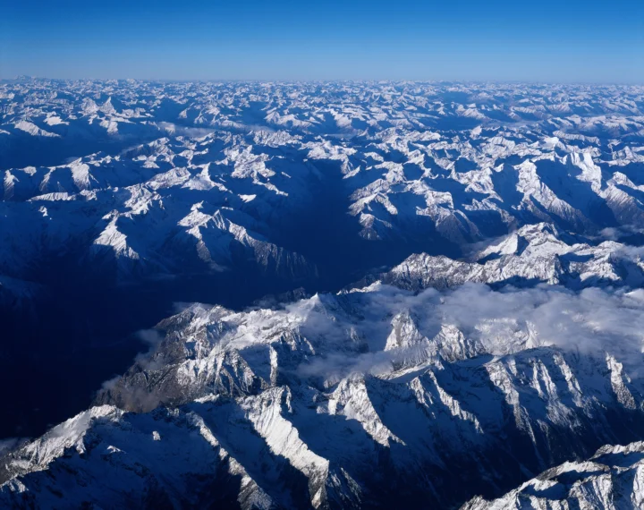 从高空俯瞰连绵起伏的雪山山脉，蓝天与云层映衬着壮阔的冰雪景色。