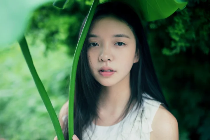 一名成年女性站在茂密绿叶之间，面向镜头微笑。
