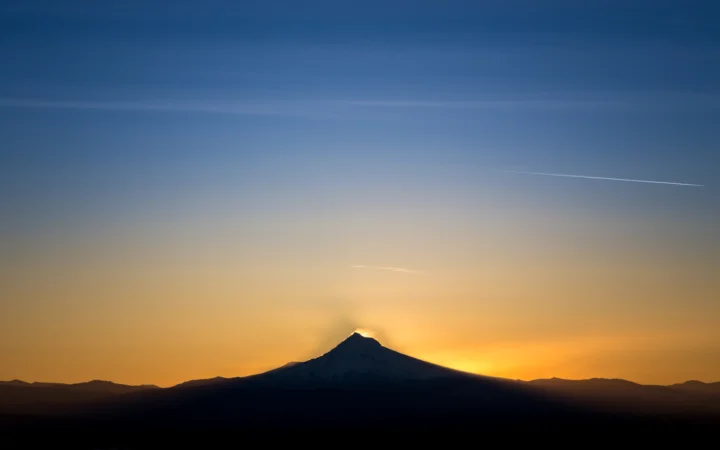 暮色天空下，一座山峰以深色剪影映衬着金橙色的夕阳余晖。