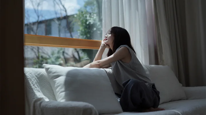 一名女子坐在窗边的沙发上，沐浴在柔和的自然光中。