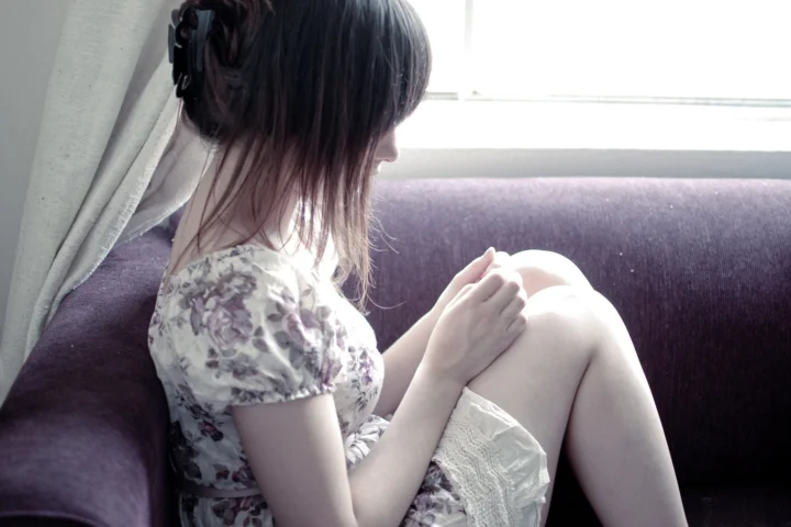 一名女子坐在窗边的紫色沙发上，穿着印花连衣裙。