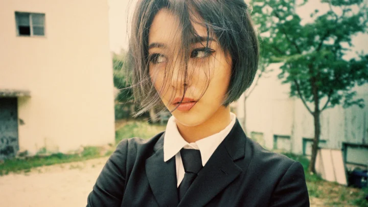 一位短发女士穿着黑色西装和白色衬衫站在户外。