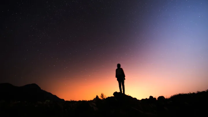 群山剪影前的地平线映着橙色日落，夜空中散布着星星。