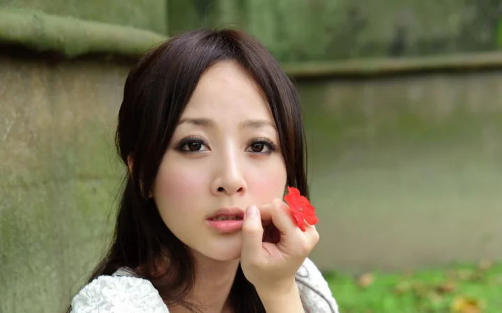 一名成年女性在户外背景前手持红色花朵靠近脸部。