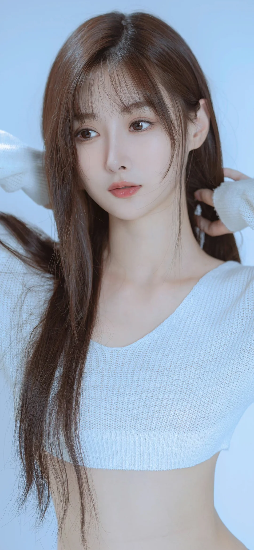 一名长发女子穿着白色针织衫，在浅蓝色背景前看向镜头。