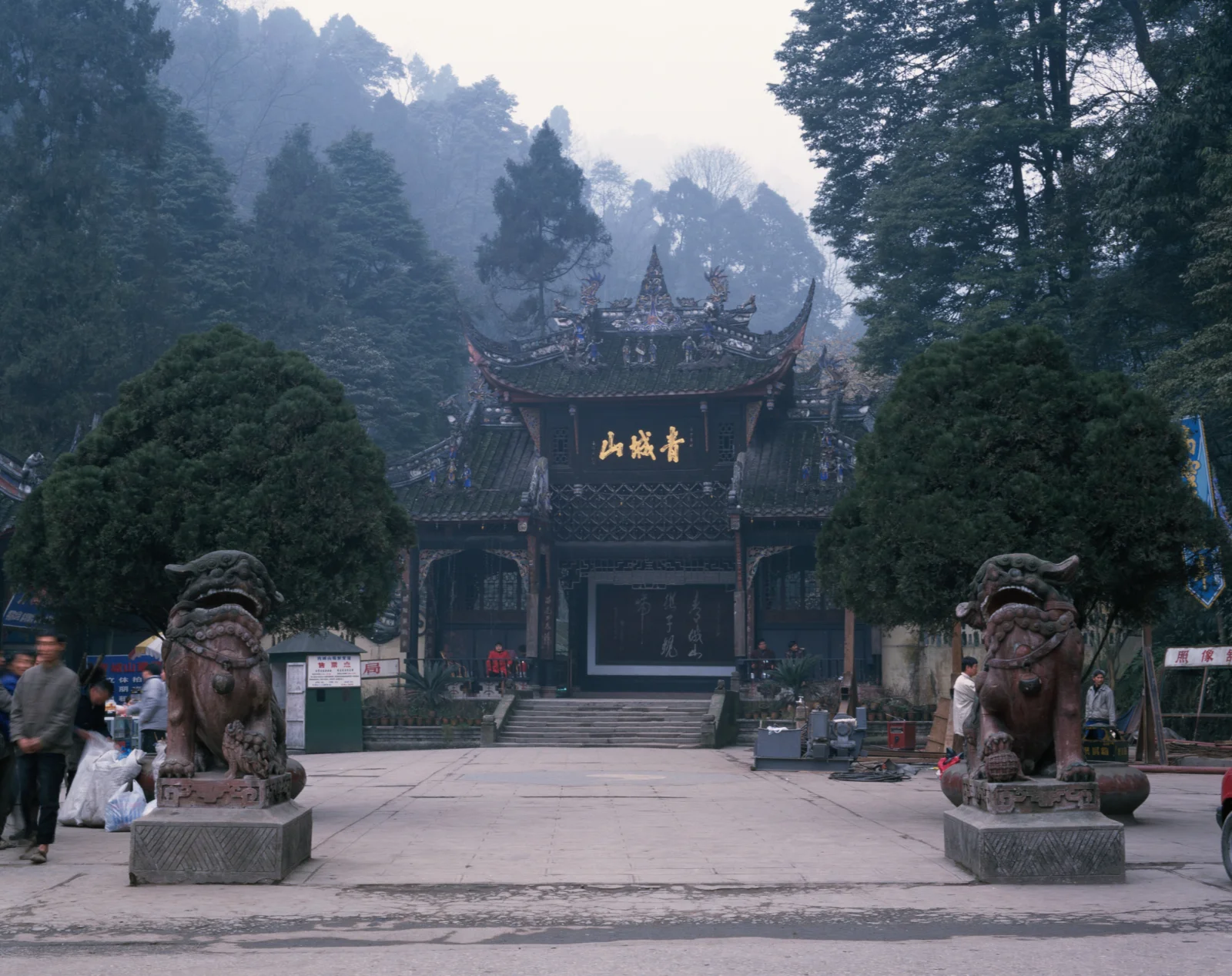 雾气笼罩的山中古寺入口前立着两尊石狮，周围被浓密树林环绕。