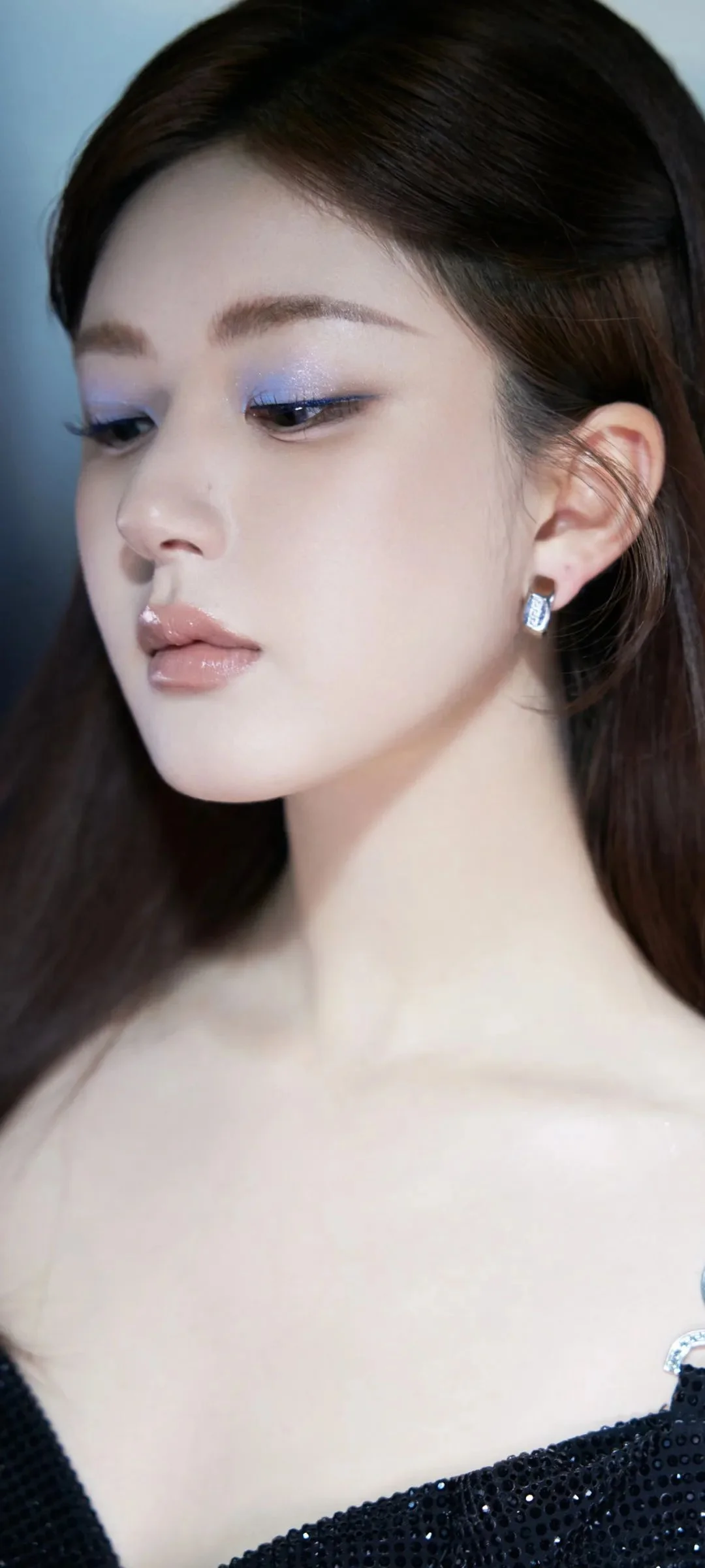 一名成年女性的近距离侧脸肖像，妆容精致，佩戴耳饰并穿着黑色亮片上衣。