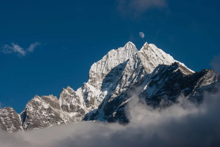 巍峨的积雪山峰耸立在云雾之上，背景是深蓝色天空。