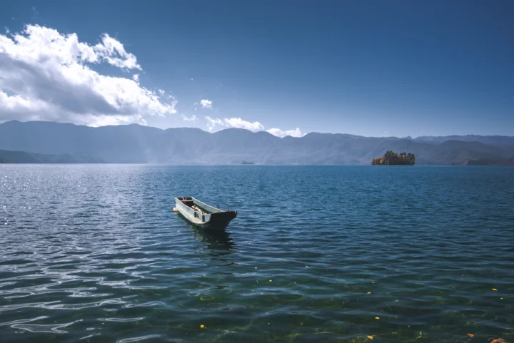 一叶小舟漂浮在湖面上，远处是群山与晴朗天空。