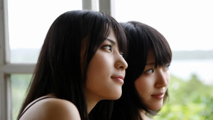 两位黑发女性并肩靠近窗边，以侧脸望向窗外。