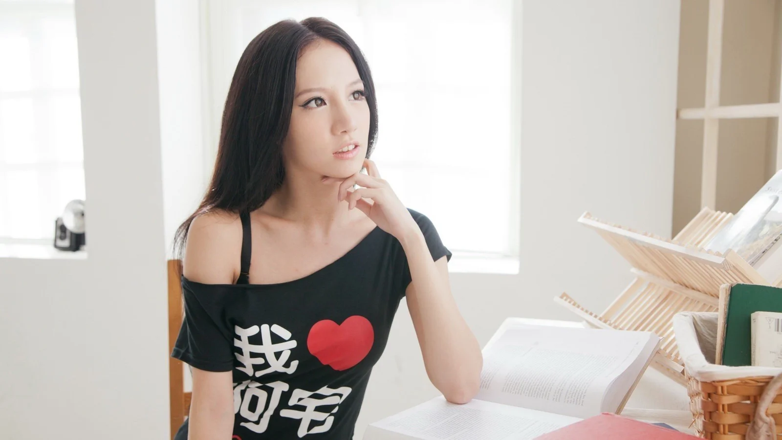 明るい窓辺で大人の女性が頬杖をつき、開いた本や収納かごが周囲に置かれています。