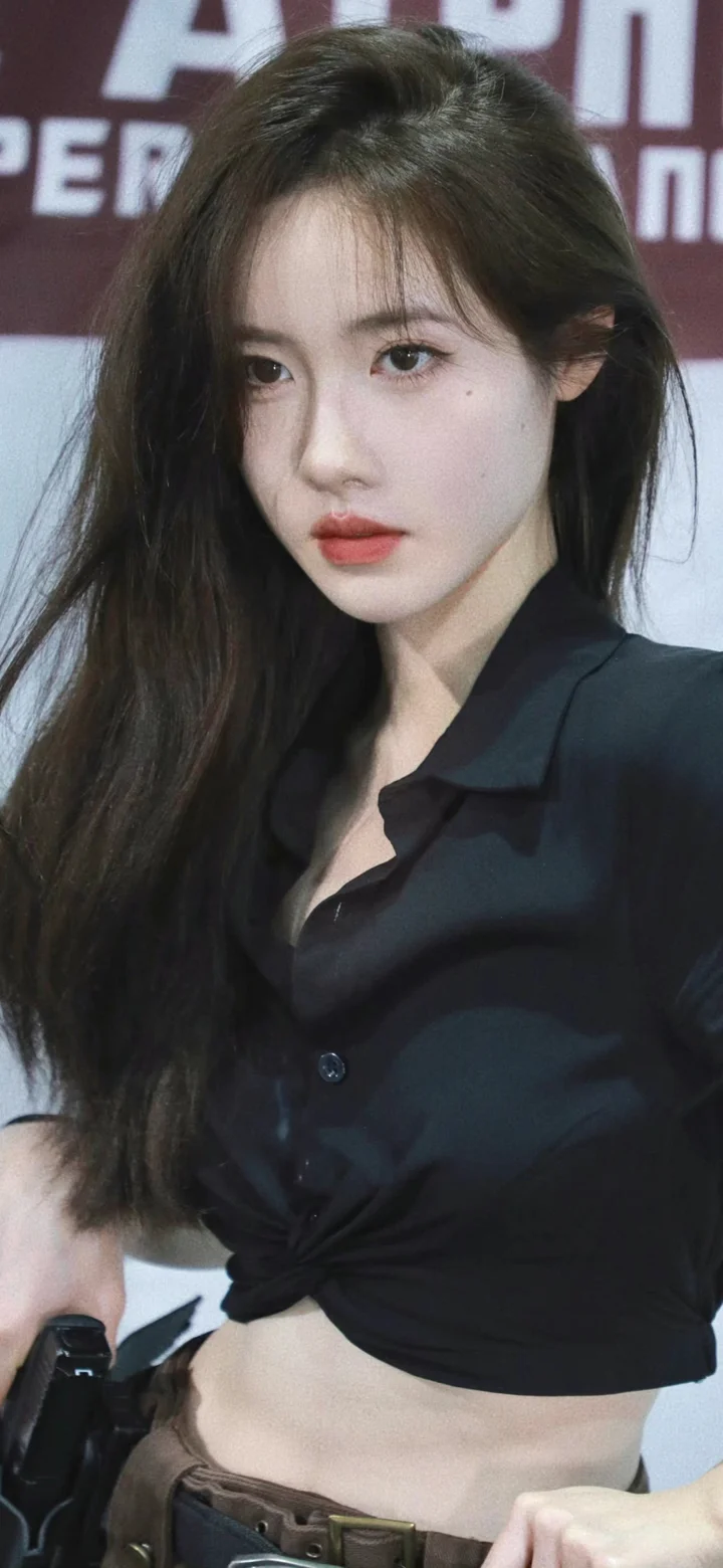一名長髮女子穿著黑色襯衫，在背景板前面向鏡頭。