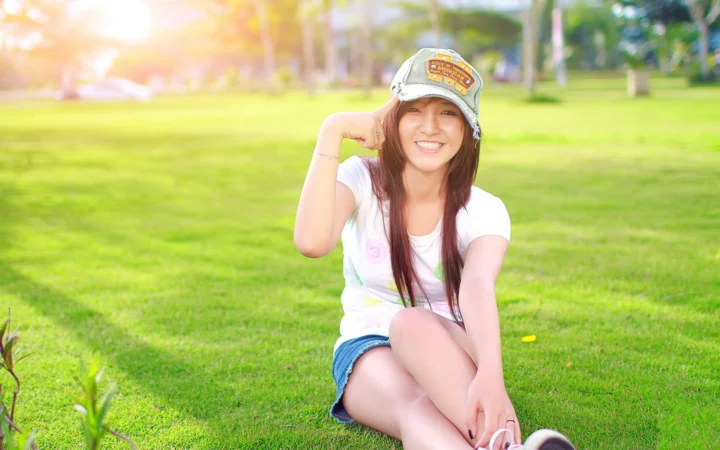一名戴帽子的成年女性坐在阳光明媚的草地上。
