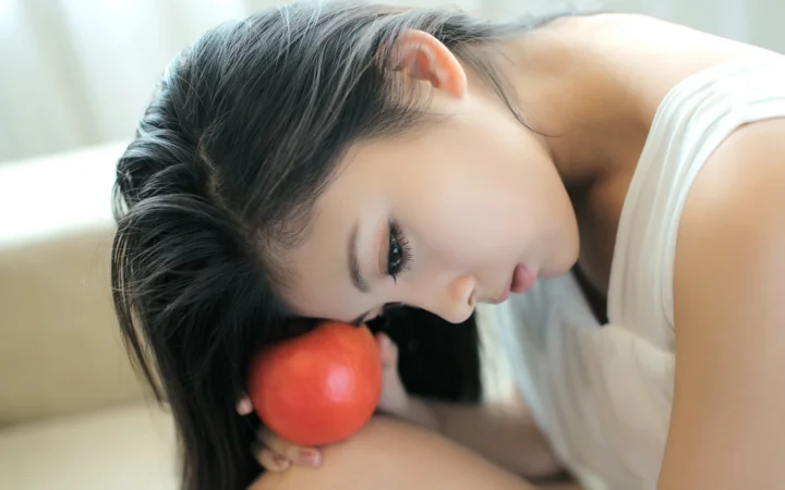 一名穿白色上衣的女子将头靠在红苹果旁边。