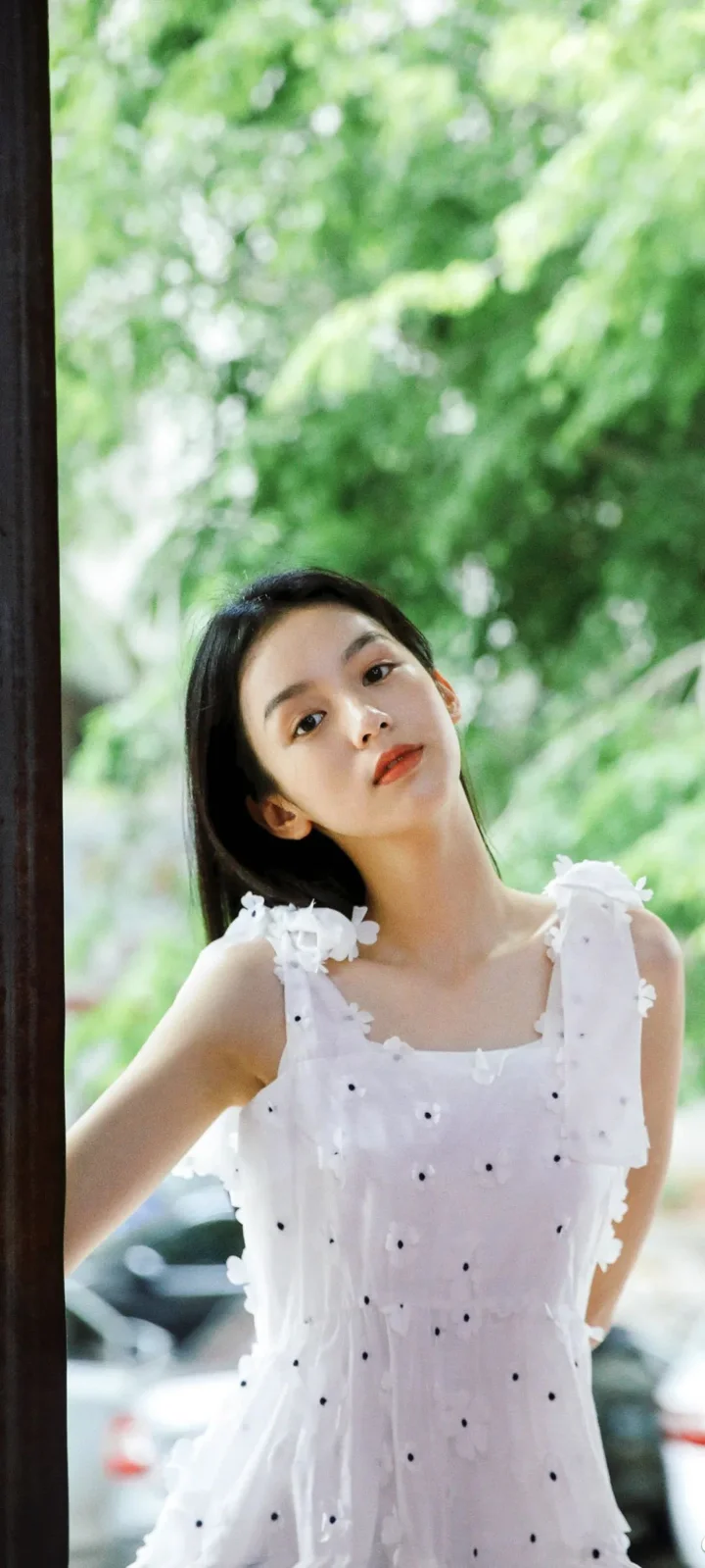 一名女子身穿白色连衣裙站在绿意盎然的户外背景前。