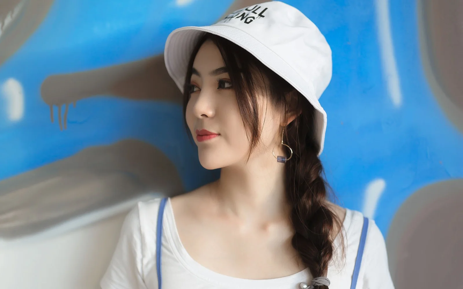 흰 모자를 쓴 여성이 파란색 배경 앞에서 옆모습을 보이고 있다.