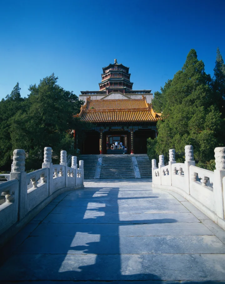 蓝天下，一座传统中式楼阁坐落在树木环绕的石桥尽头。