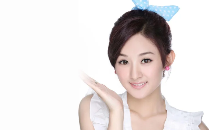 一位面带微笑、头戴蓝色蝴蝶结的女性在白色背景前摆姿势。