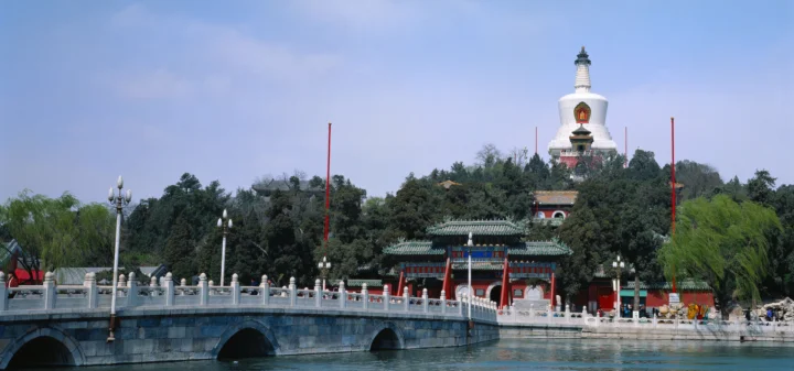 湖畔石桥前坐落着一座古寺，树林上方可见白色佛塔。
