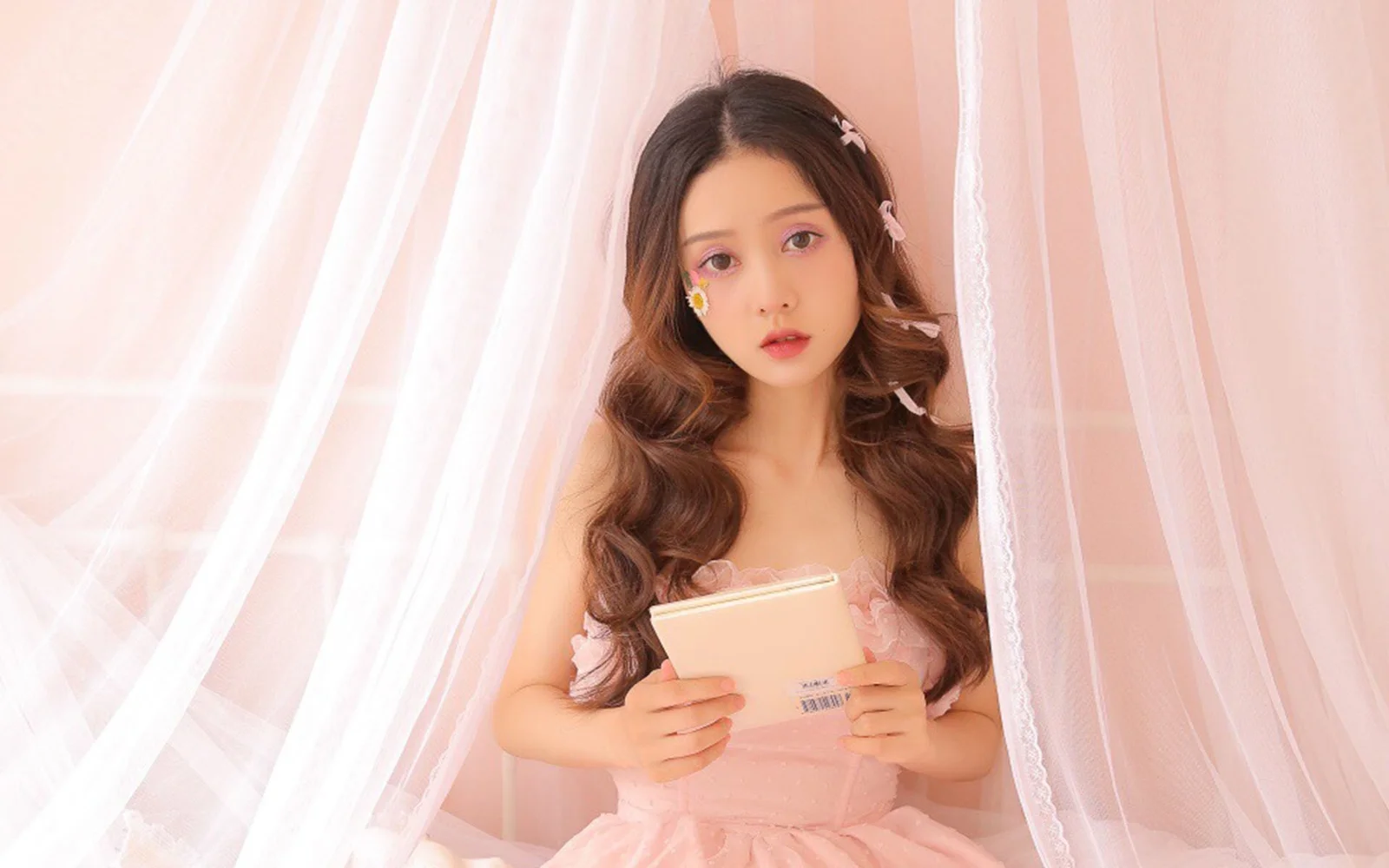一名穿粉色服装的女性手持浅色物品站在粉色窗帘前。