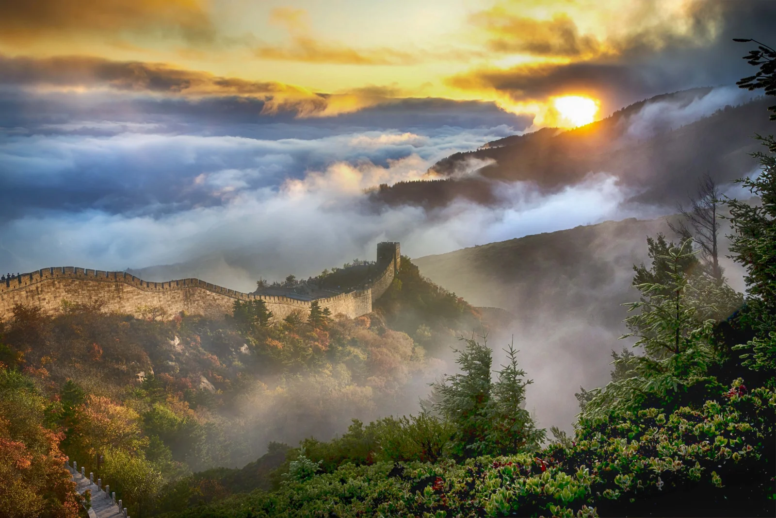 长城蜿蜒穿过山脊，云雾、群山与落日构成壮丽的风景画面。