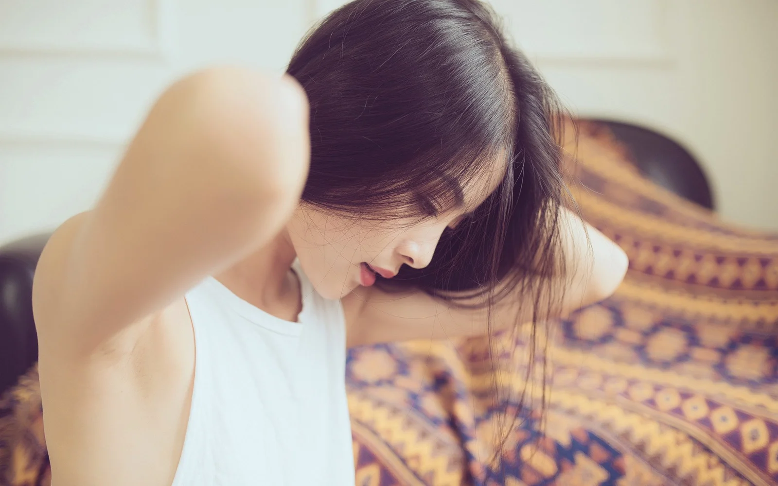 一名深色长发女性穿着白色上衣，在室内低头整理头发。