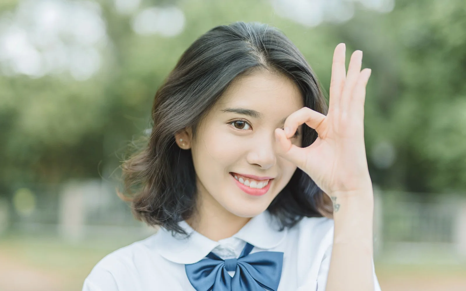 一名微笑的女性在戶外背景前用手比出圓圈手勢。