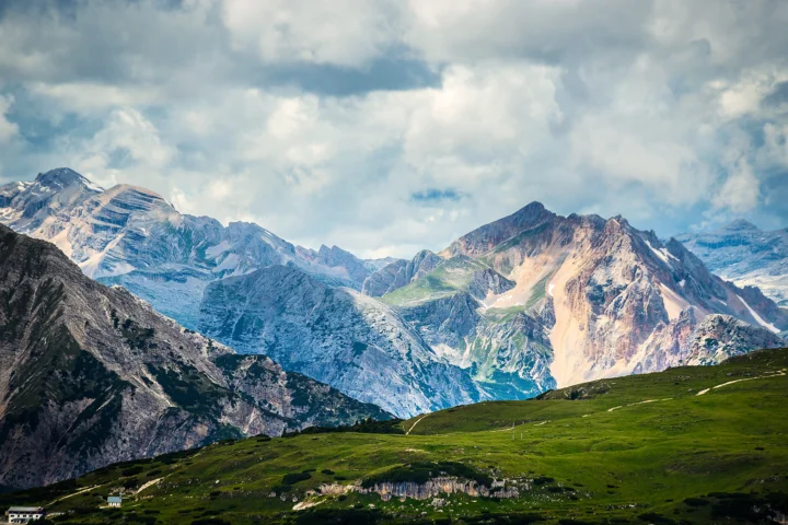 葱绿的高山草甸延伸至壮丽的雪山群峰，天空中覆盖着厚重云层。